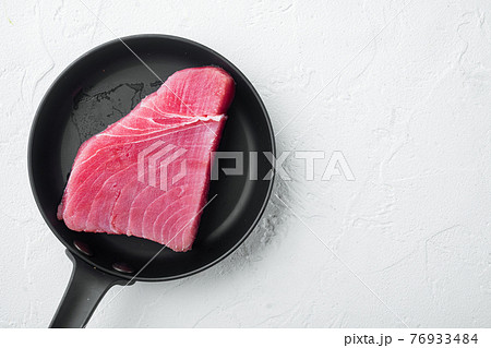 Raw tuna steak , on frying cast iron pan, on white stone background, top view flat lay Raw tuna steak , on frying cast iron pan, on white stone background, top view flat lay 76933484