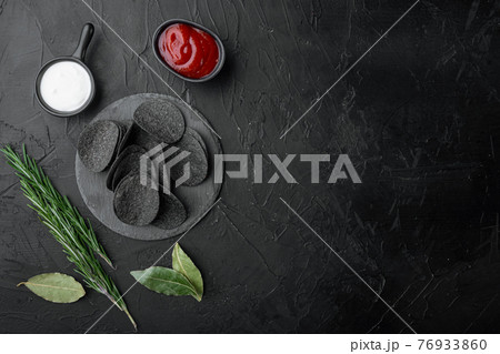 Black crispy potato chips, on black stone background, top view flat lay, with copy space for text Black crispy potato chips, on black stone background, top view flat lay, with copy space for text 76933860