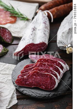 Variety of dry cured chorizo, fuet and other sausages cut in slices with herbs on old wooden table 76933864