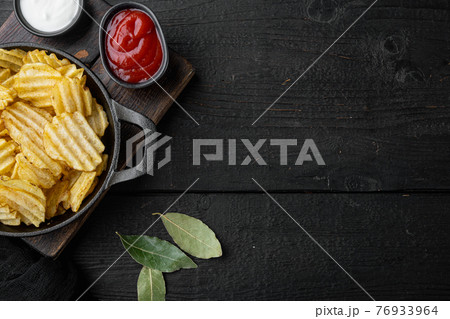 Salty potato chips snack , on black wooden background, top view flat lay, with copy space for text 76933964