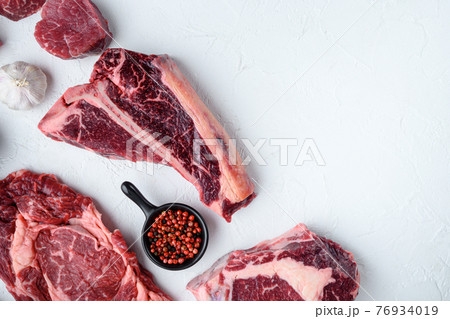 Various cuts of marbled beef meat and dry aged steaks, tomahawk, t bone, club steak, rib eye and tenderloin cuts, on white stone background, top view flat lay, with copy space for text 76934019