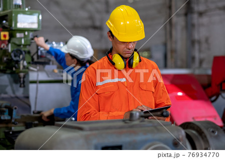 Factory worker man hold tablet and inspect the function while her co-worker work with other machine 76934770