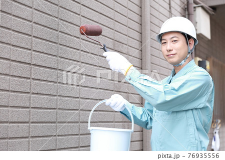 一軒家の外壁に塗装をする作業員の男性 76935556