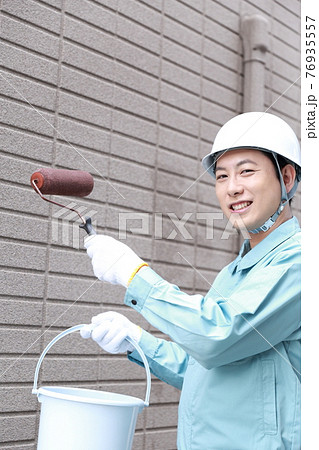 一軒家の外壁に塗装をする作業員の男性 76935557
