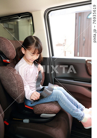 助手席に取り付けたジュニアシートでシートベルトを着用する女の子の写真素材