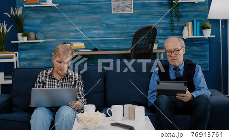 Senior man trying on tablet while his wife uses laptop 76943764