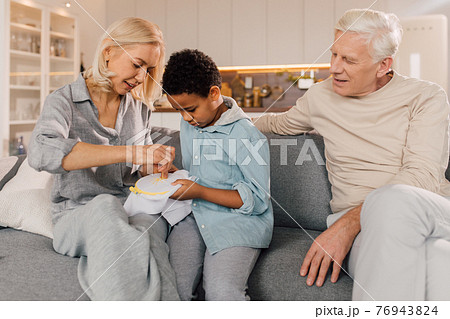 Boy asking his grandmother while she doing needlework at home Boy asking his grandmother while she doing needlework at home 76943824