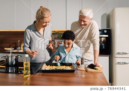 Father and mother standing at the modern kitchen and helping their multiracial son 76944341