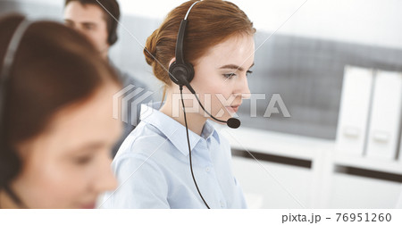 Young woman using headset and computer while talking with customers online. Group of Call center operators at work. Business concept 76951260