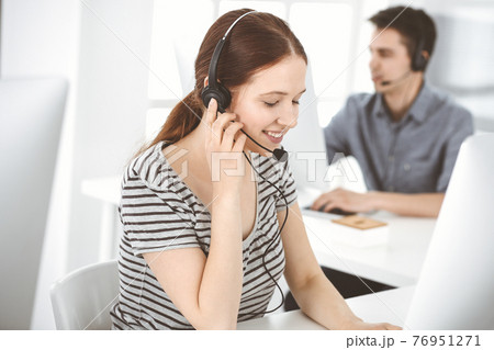 Casual dressed young woman using headset and computer while talking with customers online. Group of operators at work. Call center, business concept Casual dressed young woman using headset and computer while talking with customers online. Group of operators at work. Call center, business concept 76951271