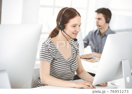 Casual dressed young woman using headset and computer while talking with customers online. Group of operators at work. Call center, business concept Casual dressed young woman using headset and computer while talking with customers online. Group of operators at work. Call center, business concept 76951273