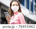 フェースマスクを付けて外で携帯を持っている若い女性 76953962