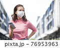 フェースマスクを付けて外で携帯を持っている若い女性 76953963