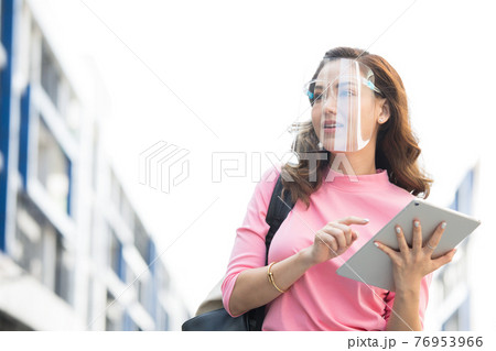 フェースシールドを付けてタブレットをもっている何かを探している女性 フェースシールドを付けてタブレットをもっている何かを探している女性 76953966