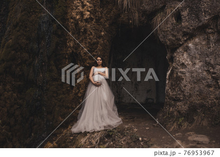 pregnant woman with a big belly in a white long dress near mountains 76953967