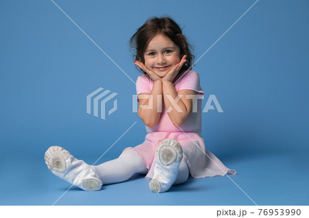Portrait of an adorable child girl ballerina cute smiling while sitting on blue background 76953990