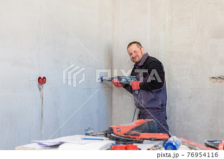 An electrician drills holes for sockets with a diamond core bit An electrician drills holes for sockets with a diamond core bit 76954116