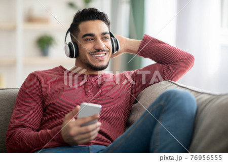 Cheerful arab man listening to music on mobile phone Cheerful arab man listening to music on mobile phone 76956555