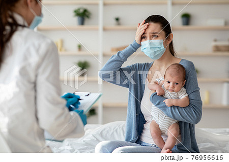 Mother In Protective Mask Holding Newborn Baby, Explaining Illness Symptoms To Doctor Mother In Protective Mask Holding Newborn Baby, Explaining Illness Symptoms To Doctor 76956616