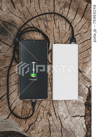 Close up of modern smartphone charges from the portable power bank on the old stump background. Modern technology concept. 76969248