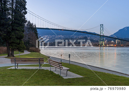Stanley Park Seawall wooden bench. Lions Gate Bridge In the background at twilight. Vancouver, British Columbia, Canada. Stanley Park Seawall wooden bench. Lions Gate Bridge In the background at twilight. Vancouver, British Columbia, Canada. 76970980
