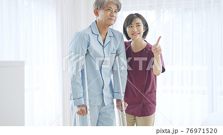 松葉杖で歩く中高年男性と介助するヘルパー女性 76971520