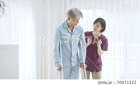 松葉杖で歩く中高年男性と介助するヘルパー女性 76971522