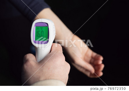 Measuring body temperature with laser thermometer on dark background Measuring body temperature with laser thermometer on dark background 76972350