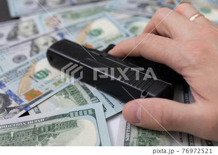 hand holding a gun lies on a pile of money hand holding a gun lies on a pile of money 76972521