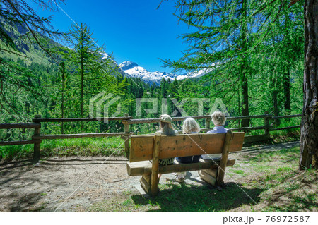 Tourists on a bench in the mountains relax while observing the view 76972587