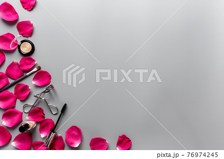 Make up accessories composition between red rose petals on grey background 76974245