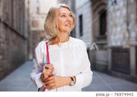 Elegant mature woman is posing in time walking on the street of old city 76974942