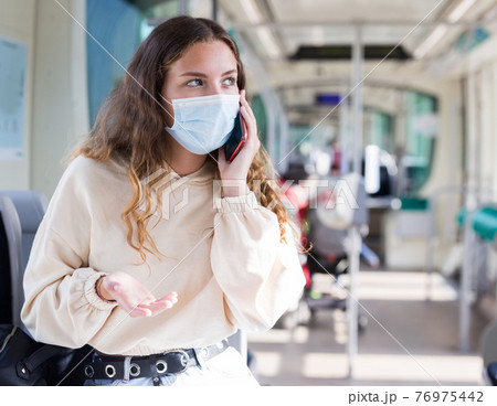 Girl in a protective mask, riding on public transport, communicates on a mobile phone Girl in a protective mask, riding on public transport, communicates on a mobile phone 76975442