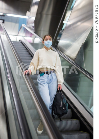 Young girl in protective face mask, standing on the escalator Young girl in protective face mask, standing on the escalator 76975821