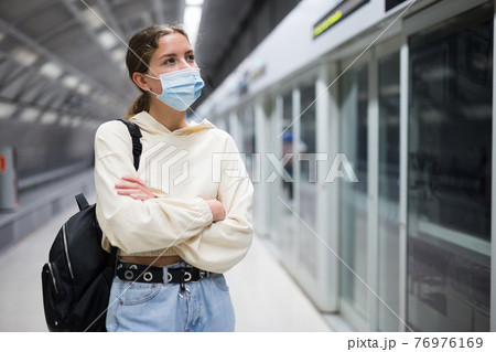 Young woman in face mask waiting for train 76976169