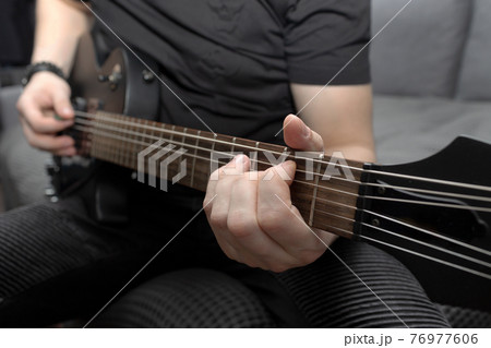 Musician playing black electric guitar. Guitar fretboard close-up. Learning to play the guitar. Self-development at home Musician playing black electric guitar. Guitar fretboard close-up. Learning to play the guitar. Self-development at home 76977606