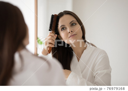 Girl in bathrobe brushing smooth brown hair at mirror 76979168