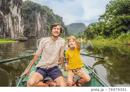 Dad and son tourists in boat on the lake Tam Coc, Ninh Binh, Viet nam. It's is UNESCO World Heritage Site, renowned for its boat cave tours. It's Halong Bay on land of Vietnam. Vietnam reopens borders 76979391