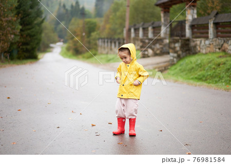 Playful girl wearing yellow raincoat while jumping in puddle during rainfall Playful girl wearing yellow raincoat while jumping in puddle during rainfall 76981584