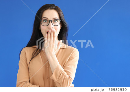 Surprised woman with glasses covers her mouth with her hand Surprised woman with glasses covers her mouth with her hand 76982930