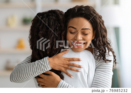 Loving black mother hugging her daughter, home interior Loving black mother hugging her daughter, home interior 76985232
