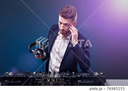 Man DJ in dark suit play music on a Dj's mixer. Studio shot. Dark blue background Man DJ in dark suit play music on a Dj's mixer. Studio shot. Dark blue background 76985255