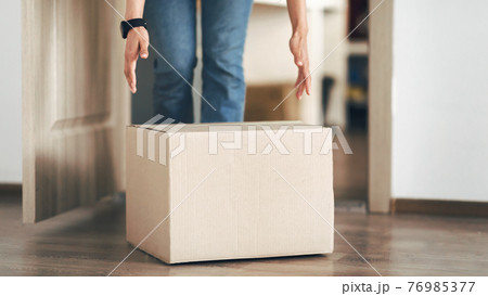 Unrecognizable person picking cardboard box up from the floor Unrecognizable person picking cardboard box up from the floor 76985377