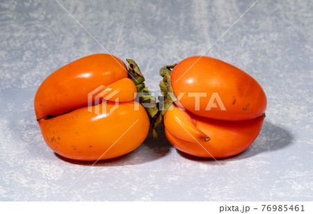 Two ugly orange persimmons are lying on light grey textured backdrop close up. Zero waste food concept. Fresh healthy organic fruits. Reasonable sustainable consumption of food. 76985461