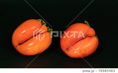 Two non-standard ugly ripe orange persimmons on black background close up. Fresh natural healthy organic fruits. Zero waste food, reasonable and sustainable consumption concepts. 76985463