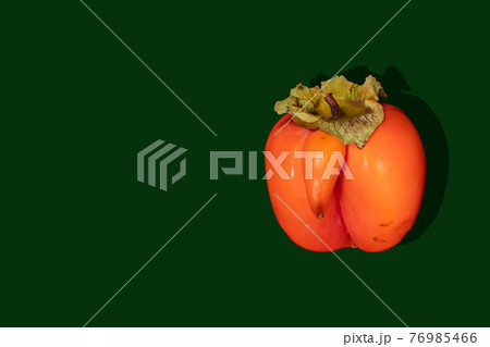 One ugly ripe orange persimmon with shadow on dark green background. Fresh natural healthy organic fruits. Zero waste food concept. Reasonable and sustainable consumption. Copy space, close up. 76985466