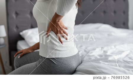Woman with side back pain sitting on bed at home 76985526