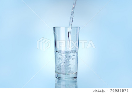 transparent glass is filled with water from a stream of liquid stream, drinkware on a blue background with copy space. 76985675