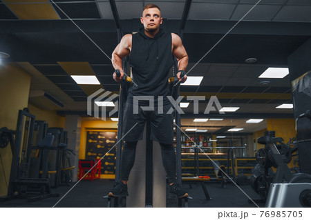 Strong muscular man doing push-ups on uneven bars in gym. Workout lifestyle concept. 76985705