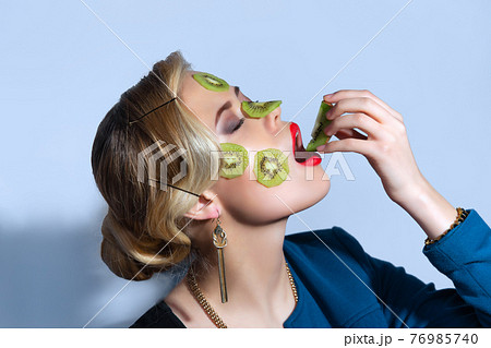 Fashion photo of woman posing with slices of kiwi on her face 76985740